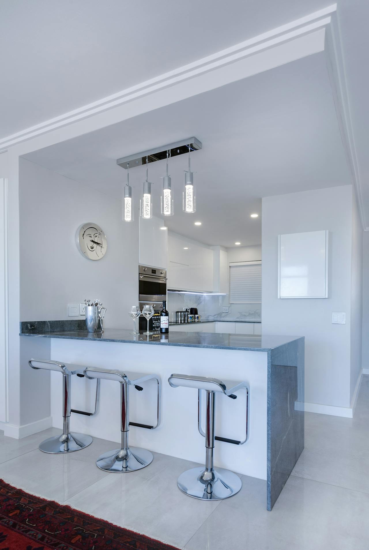 Open-plan kitchen with a peninsula, bar seating and pendant lights facing the living area